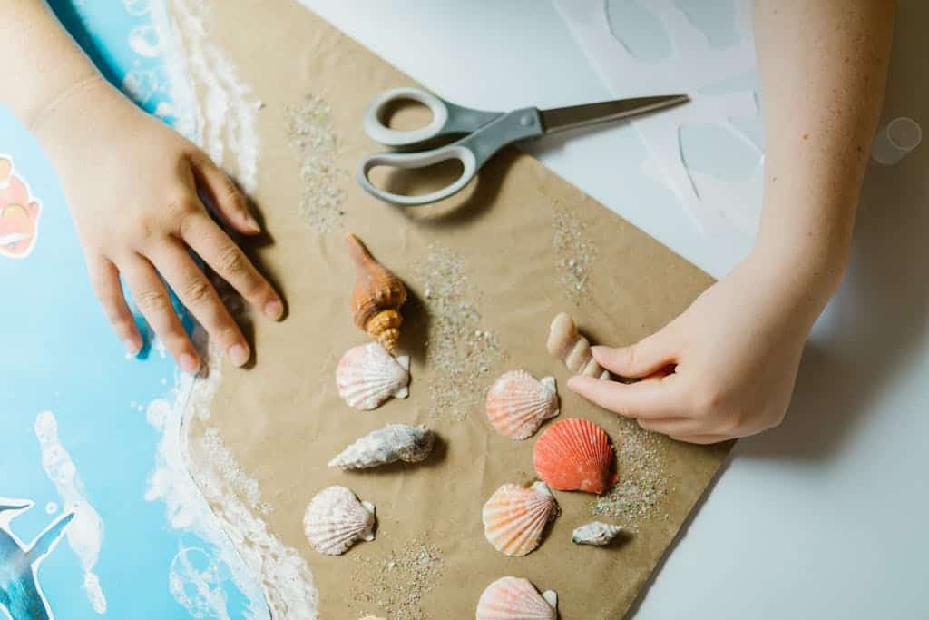 Hands arranging seashells on paper, engaging in a creative craft project.
