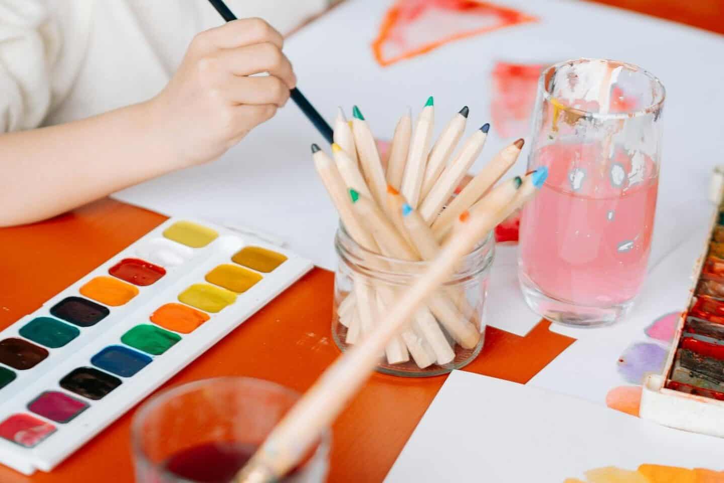 A young girl painting with watercolors at a table, showcasing her artistic creativity.