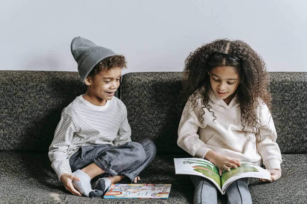 Siblings reading a picture book together indoors, fostering a love of literature.