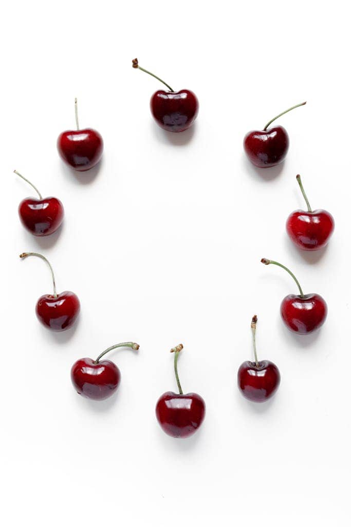 Top view of ripe cherries arranged in a circle on a white background, creating negative space.